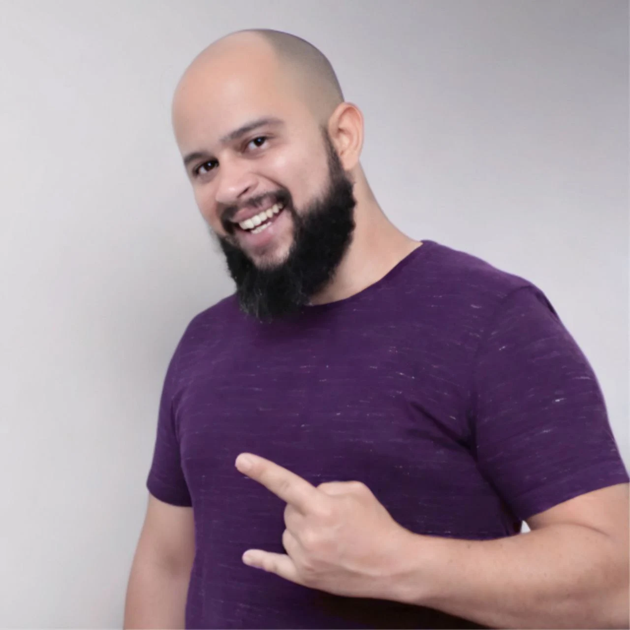 Ilustração digital de um homem com barba cheia e careca, vestindo uma camiseta roxa com um pequeno logotipo branco no peito.